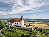 Ein weißes Kirchengebäude mit rotem Dach auf einem Hügel, umgeben von Feldern.