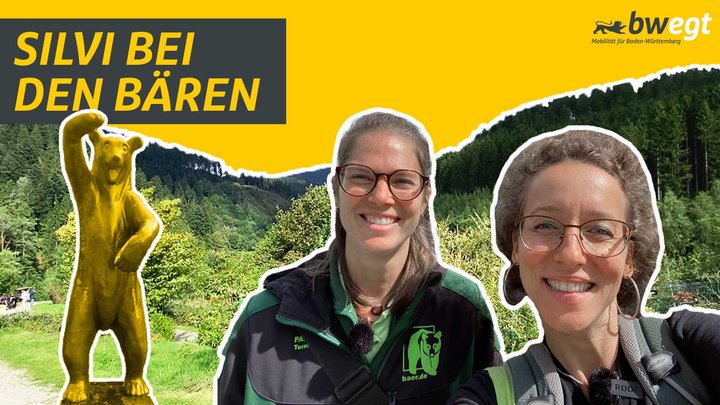 Zwei Frauen stehen vor einem Wald mit Bärenstatue.