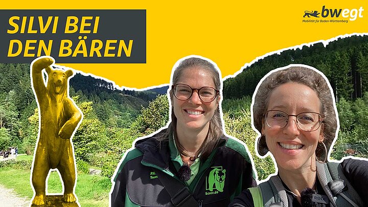 Zwei Frauen stehen vor einem Wald mit Bärenstatue.
