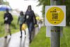 Ein QR-Code unter dem bwegt-Logo ist an einem Schild befestigt, unscharf im Hintergrund ist eine wandernde Menschengruppe mit Regencapes und -schirmen.