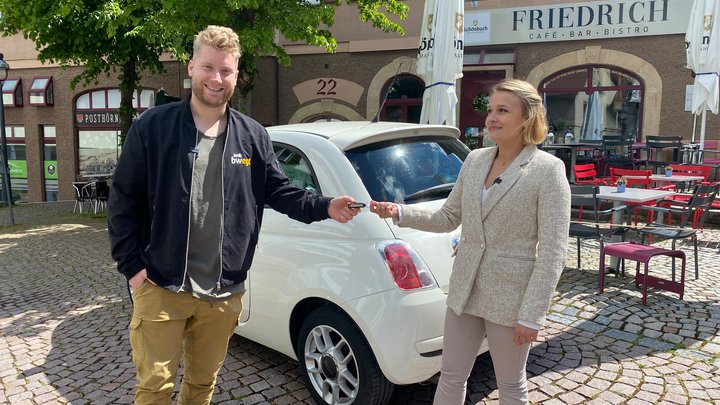 Mann nimmt vor einem Auto stehende den Schlüssel der Fahrerin entgegen.