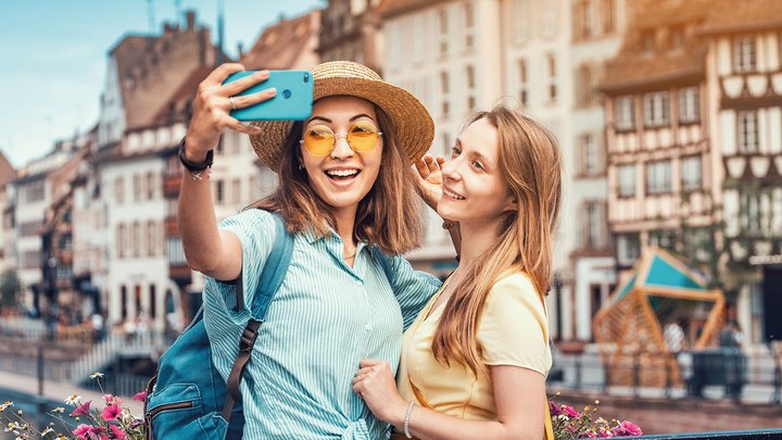 Zwei junge Mädchen machen ein Selfie von sich vor einer Häuserfassade