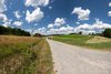 Ein langer Weg zieht sich vom Vordergrund des Bildes bis zum Horizont. Auf beiden Seiten des Weges erstrecken sich Wiesen.