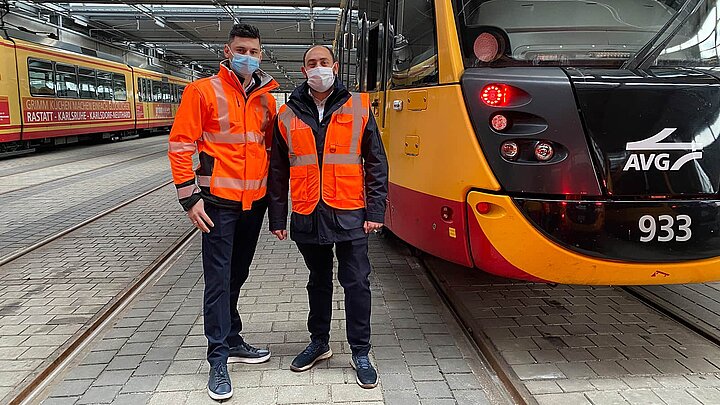 Zwei Lokführer stehen neben einer Straßenbahn der AVG.