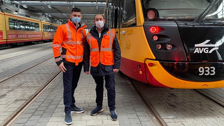 Zwei Lokführer stehen neben einer Straßenbahn der AVG.