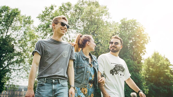 Drei junge Menschen laufen gemeinsam durch einen grünen Park.