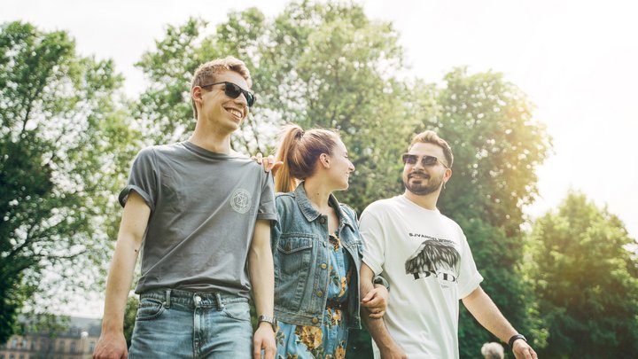 Drei junge Menschen laufen gemeinsam durch einen grünen Park.