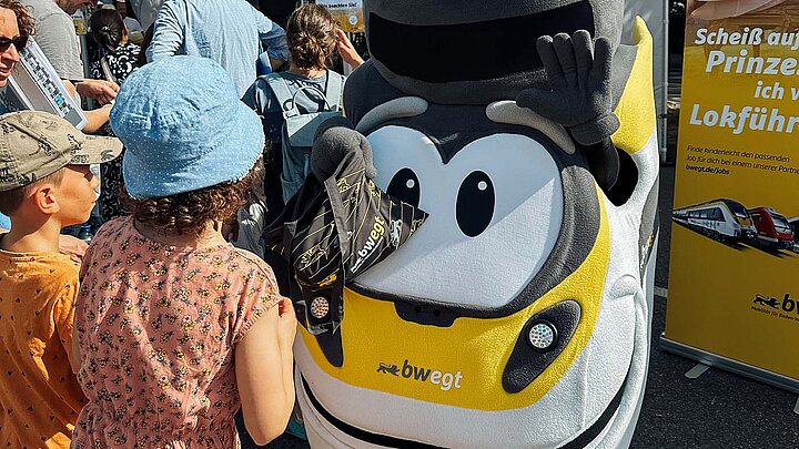 Auf einer Veranstaltung winkt das bwegt-Maskottchen zwei Kindern zu