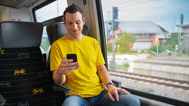 Ein Mann sitzt in einem bwegt-Zug und schaut auf sein Smartphone