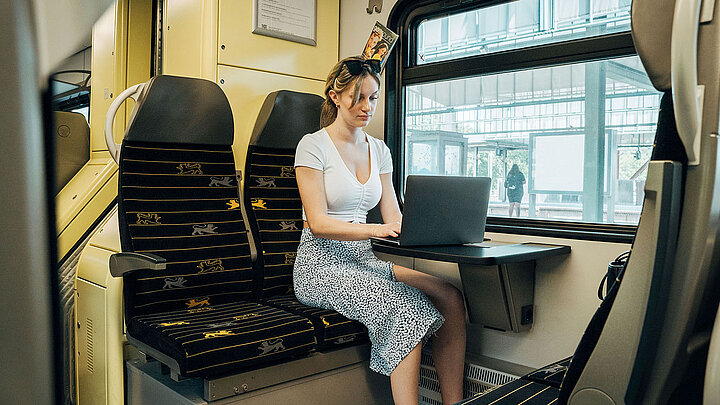 Eine Frau arbeitet während einer Bahnfahrt an ihrem Laptop