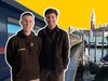 Zwei junge Männer stehen vor einem Nachtzug, im Hintergrund ist eine Kulisse aus Venedig zu erkennen.