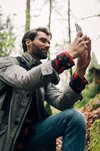 Ein junger Mann in Wanderkleidung fotografiert mit seinem Handy einen Lost-Place im Wald