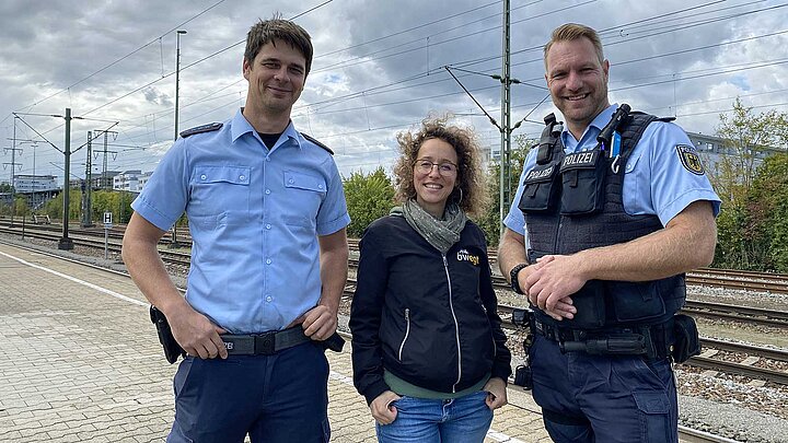 Eine Frau steht zwischen zwei Polizisten am Bahngleis.