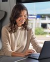 Eine Geschäftsfrau sitzt im bwegt-Zug und schaut freudig auf ihr Laptop