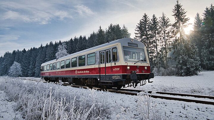 Historische Bahn in weiß und rot fährt durch eine Winterlandschaft.