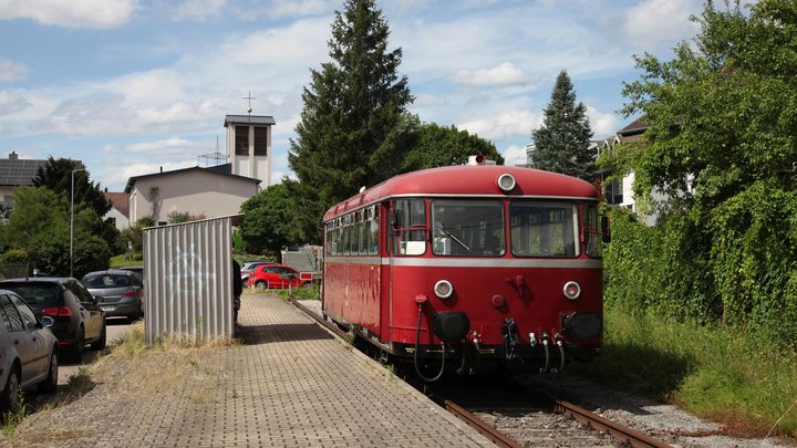 Ein historischer Schienenbus fährt an eine Haltestelle, an der er anhält.