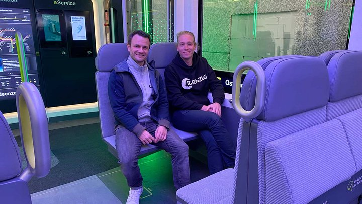 Zwei Männer sitzen in einem sehr modern aussehenden Zug.