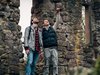 Zwei junge Männer stehen in einer Burgruine und blicken nach oben.