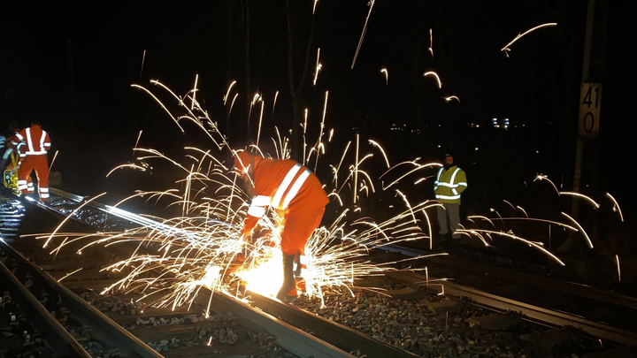 Mann in Warnanzug schweißt nachts an einem Bahngleis. Funken sprühen in alle Richtungen.