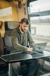 Jüngerer Mann sitzt in einem bwegt-Zug, arbeitet fokussiert am Laptop mit Kopfhörern in den Ohren.