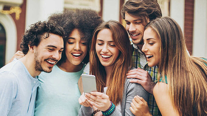 Eine Gruppe junger Menschen schaut gemeinsam auf ein Smartphone
