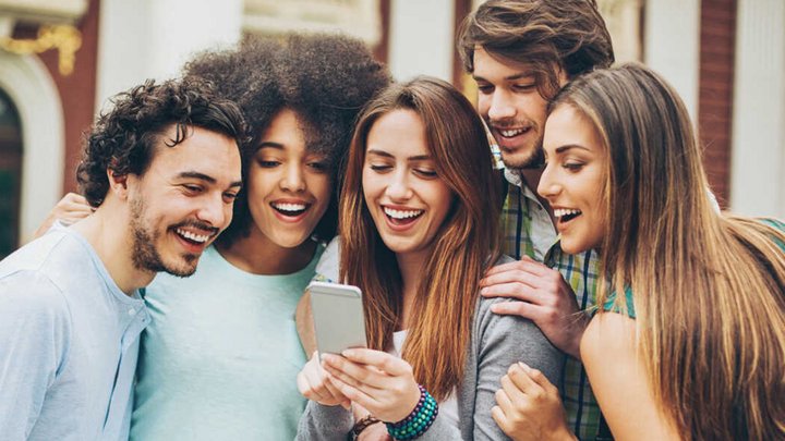 Eine Gruppe junger Menschen schaut gemeinsam auf ein Smartphone