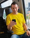 Ein Mann sitzt mit gelben Shirt in einem Zug und schaut auf sein Smartphone