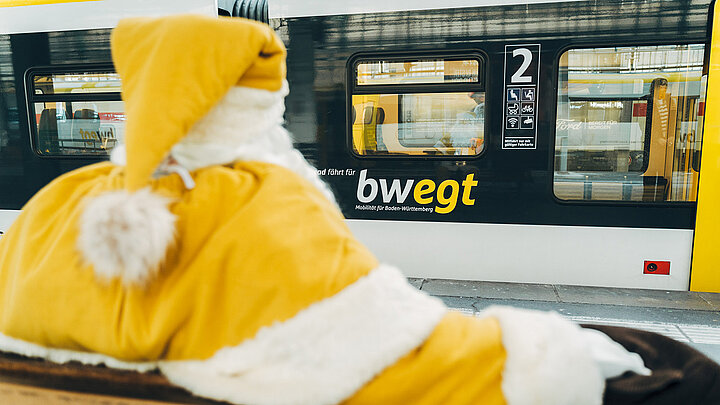 Auf einer Bank am Bahngleis wartet ein gelb verkleideter Weihnachtsmann
