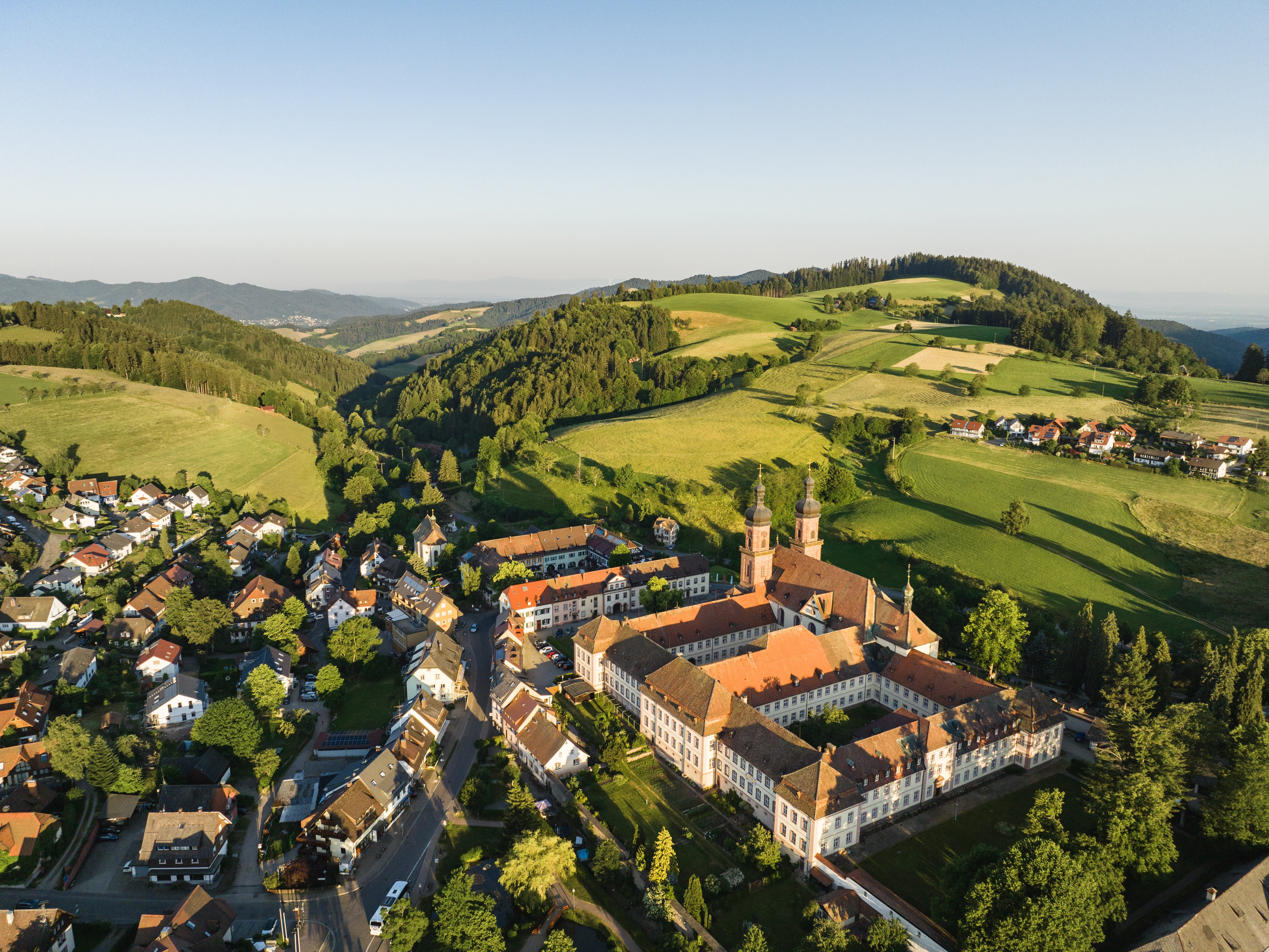Blick von oben auf ein Dorf, das umgeben ist von grünen Wiesen und Wäldern.