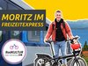 Junger Mann mit Fahrrad steht vor einer Bahn.