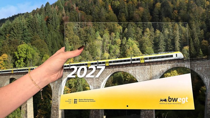 Eine Hand hält einen Kalender mit einem Zug-Motiv, dahinter ist ein Wald