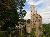 Kleines beiges Schloss thront auf einem Felsen.