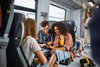 Eine Gruppe Jugendlicher sitzt zusammen in einem Vierer in der Bahn. Die zwei der Kamera zugekehrten Personen schauen lachend auf ein Smartphone.