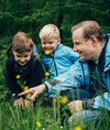 Vater zeigt seinen zwei Söhnen in der Natur Blumen.