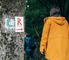 Frau geht im Wald an einem Zeichen mit einem roten R vorbei.