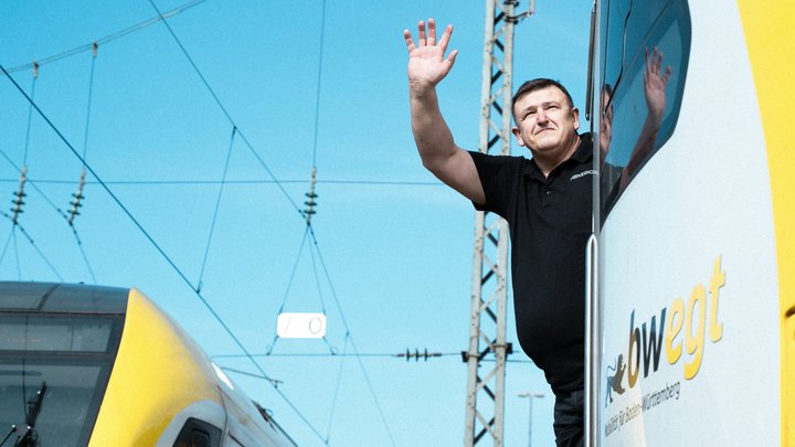 Ein Mann schaut aus einem bwegt Zug und winkt.