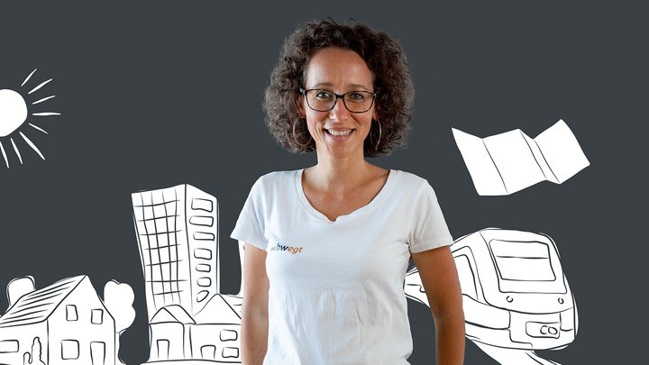 Frau steht vor einer Grafik, auf der eine Stadt, Zug und ein Plan abgebildet sind.