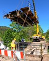 Kran hebt einen Brückenteil in die Höhe an einer Bahnbaustelle.
