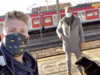 Zwei Männer stehen mit einem Hund am Bahnhof.