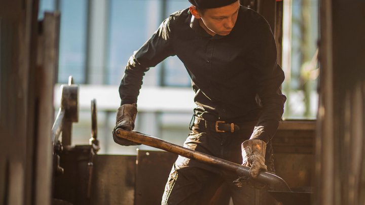Junger Mann in schwarzer Kleidung schippt im Zug Kohle.