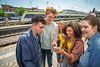 Vier junge Menschen stehen lachend auf einem Bahnsteig und schauen gemeinsam auf ein Smartphone. Im Hintergrund ist ein moderner bwegt-Regionalzug zu sehen.