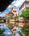 Mittelalterliche Fachwerkhäuser spiegeln sich in einem mit Geranien geschmückten Kanal.