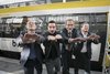 Vier Personen stehen vor einem Zug und halten ihre Hände in Vorbereitung auf eine Laola-Welle nach vorne.