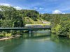 Ein bwegt-Zug fährt über eine Flussbrücke inmitten einer grünen Landschaft