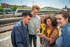 Vier junge Menschen stehen lachend auf einem Bahnsteig und schauen gemeinsam auf ein Smartphone. Im Hintergrund ist ein moderner bwegt-Regionalzug zu sehen.