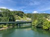 Ein bwegt-Zug fährt von rechts kommend über eine Brücke, unter der Brücke verläuft ein Fluss, die Donau, der Himmel ist blau, hinter und neben dem Zug sind Büsche und Bäume zu erkennen 