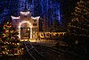 Eingang eines Bergwerks verziert mit Lichterketten und Schmuck, die am Abend leuchten. Auch die Tannen und Wagen drumherum sind geschmückt.