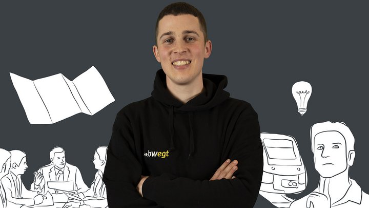 Junger Mann steht vor einer Grafik, auf der Menschen, ein Zug und ein Plan abgebildet sind.