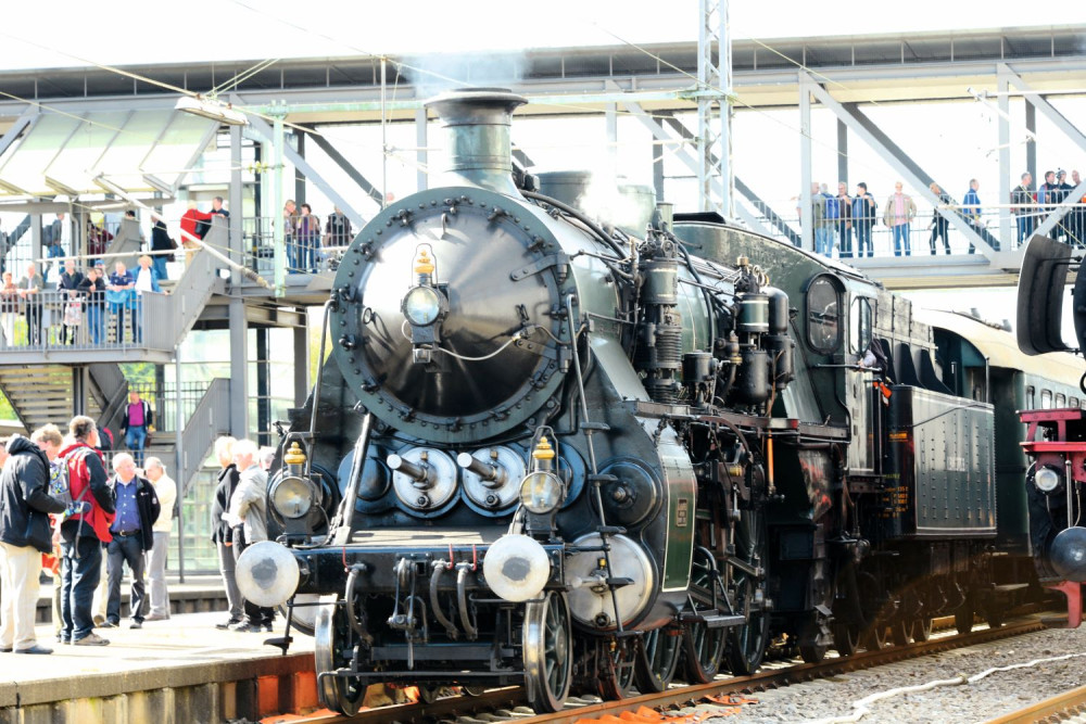Eine schwarze historische Dampflok steht an einem Bahnhof