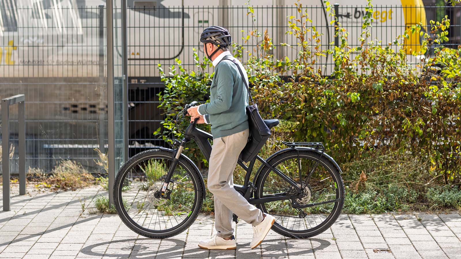 Ein Mann läuft mit seinem Fahrrad und Helm am Bahnhof entlang